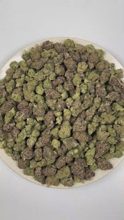 PUFFY Reese's Pieces is an indica-dominant hybrid THCa strain emerging from the intricate fusion of Riot Berry OG × Blueberry Muffin × P-91. The aroma opens with rich notes of roasted nuts and decadent chocolate, layered with a warm, doughy sweetness. Visually, dense forest green buds with purple hues and fiery orange pistils are coated in sticky trichomes. Consumers often report a euphoric cerebral boost that fosters a deeply relaxed state while helping melt away stress and anxiety. 