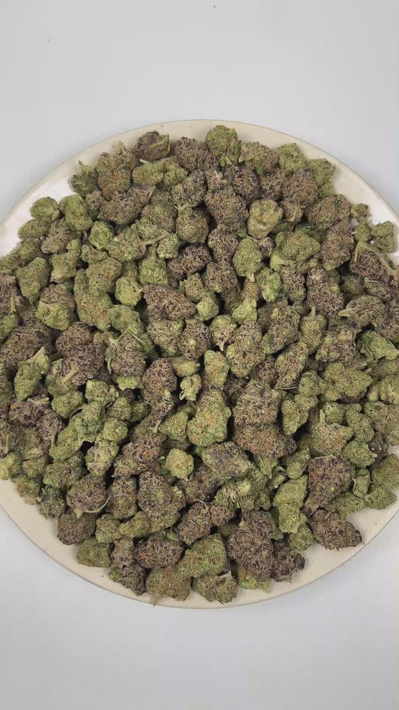 PUFFY Reese's Pieces is an indica-dominant hybrid THCa strain emerging from the intricate fusion of Riot Berry OG × Blueberry Muffin × P-91. The aroma opens with rich notes of roasted nuts and decadent chocolate, layered with a warm, doughy sweetness. Visually, dense forest green buds with purple hues and fiery orange pistils are coated in sticky trichomes. Consumers often report a euphoric cerebral boost that fosters a deeply relaxed state while helping melt away stress and anxiety. 